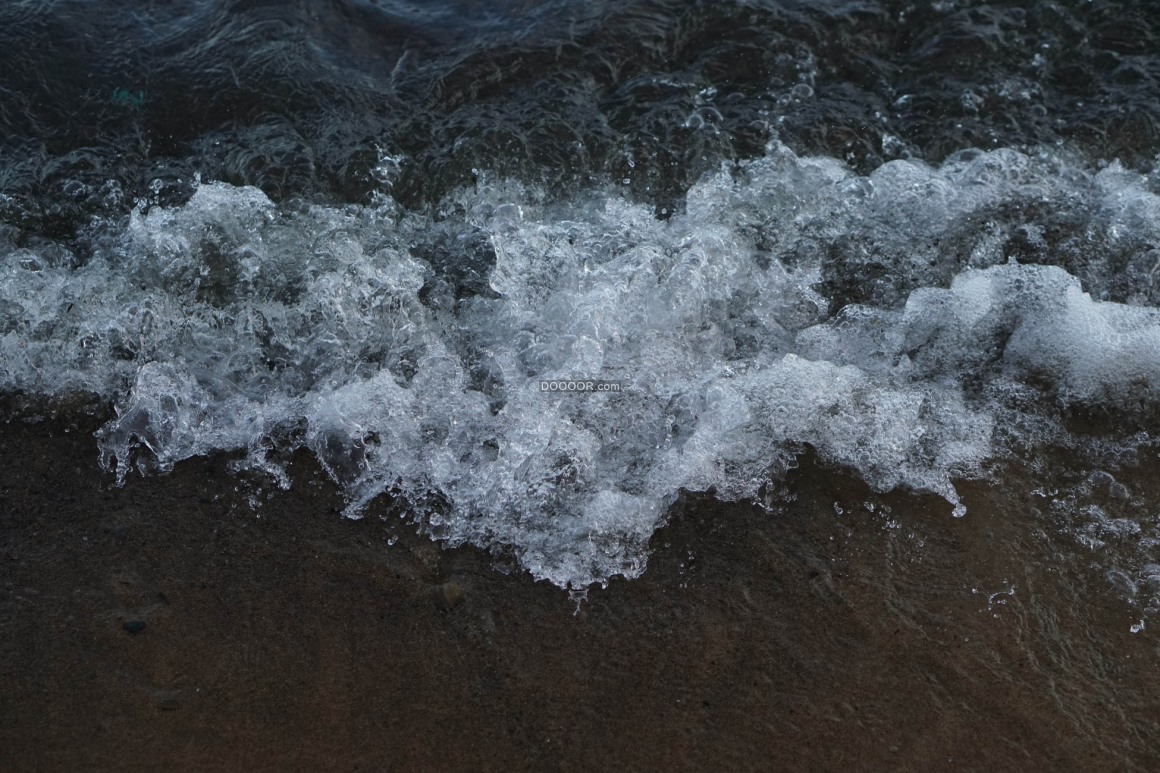 01222_海岸边的海水晶莹透彻冲向岸边的砂石溅起晶莹的浪花.jpg