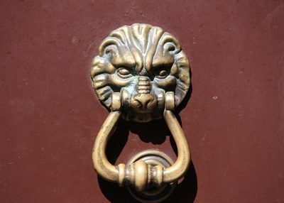 一扇朱红色的中国特色油漆大门上上面镶着一个铜质狮子头门环建筑素材设计